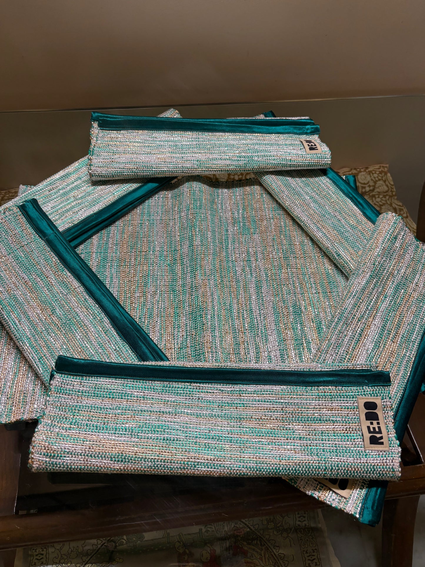 A set of woven zippered pouches in a textured teal, mint, and cream pattern, arranged on a dark wooden table. The brand name 'REBO' is visible on a small black label sewn onto the front of the pouches.